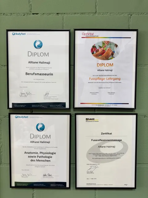 Vier gerahmte Diplome und Zertifikate von Alltane Halimaji an der grünen Praxiswand: Berufsmasseurin, Fusspflege, Anatomie und Fussreflexzonenmassage