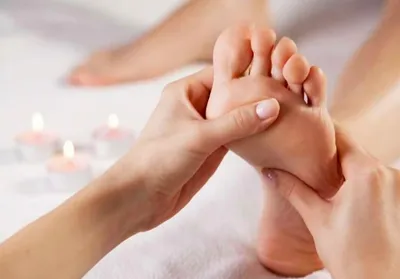 Fussreflexzonenmassage: Daumen drückt sanft auf die Reflexzonen der Fusssohle, im Hintergrund brennende Teelichter
