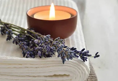 Ruhige Stimmung zur Ganzkörper-Energiemassage: brennende Kerze und Lavendelzweige auf einem weissen Tuch