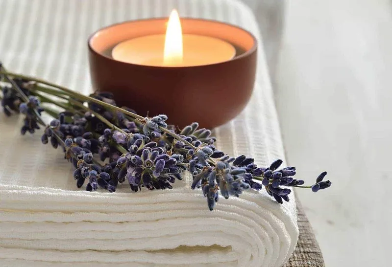 Ruhige Stimmung zur Ganzkörper-Energiemassage: brennende Kerze und Lavendelzweige auf einem weissen Tuch